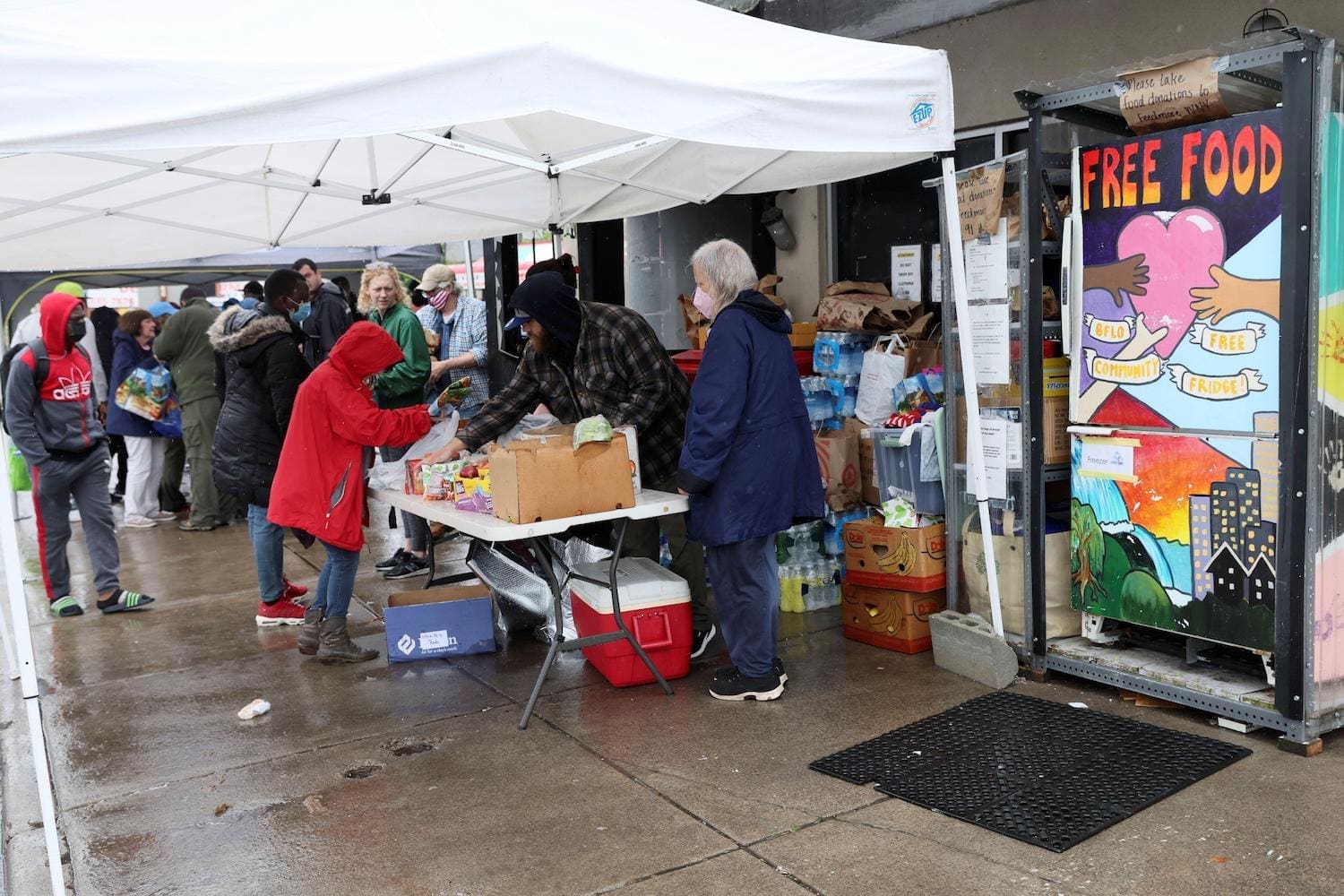 image of volunteers collecting food donations. it is raining so they are under a tent